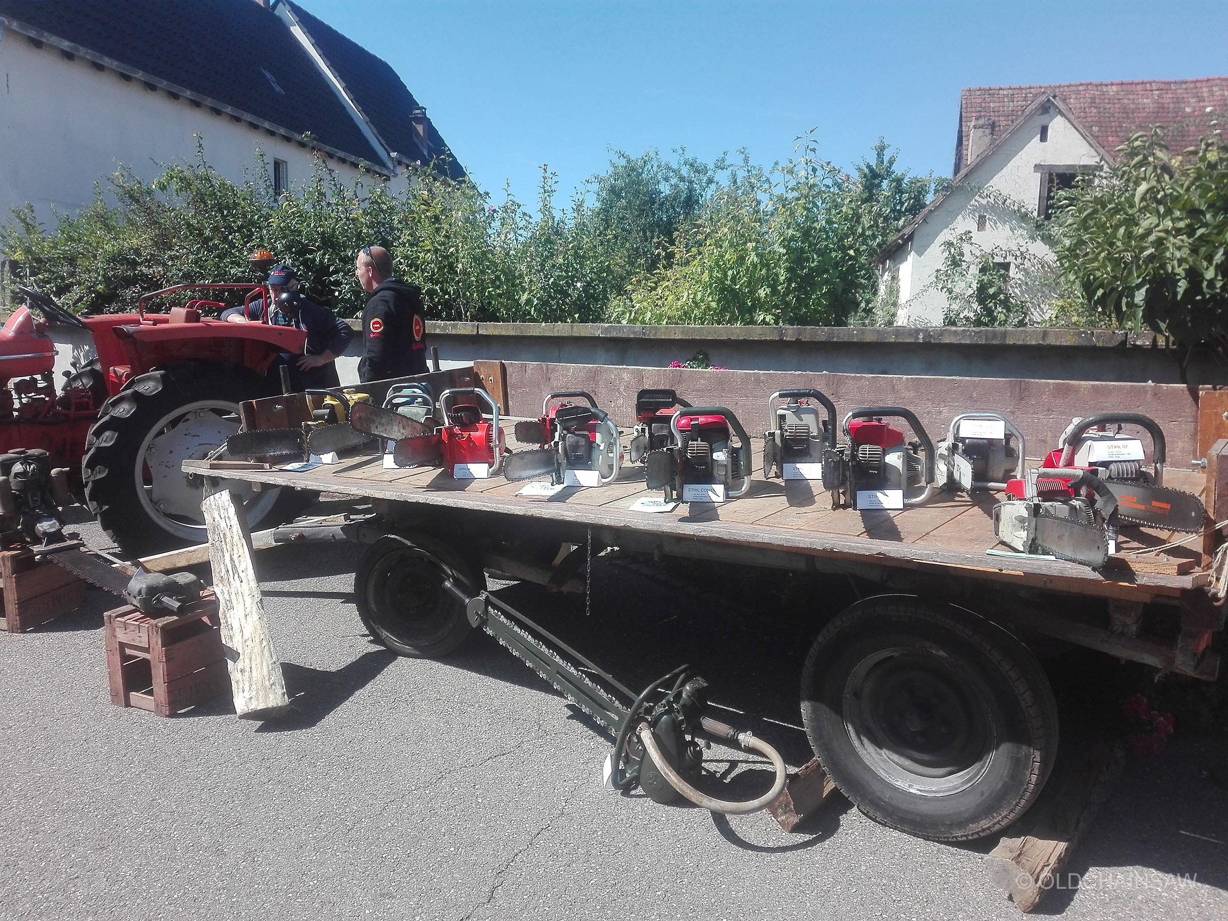 Une partie des quinze tronçonneuses exposées sur la remorque prêtée par l’association. Les machines sont accompagnées de petites fiches d’identification, tandis que les modèles les plus imposants sont présentés au sol sur des caisses en bois.